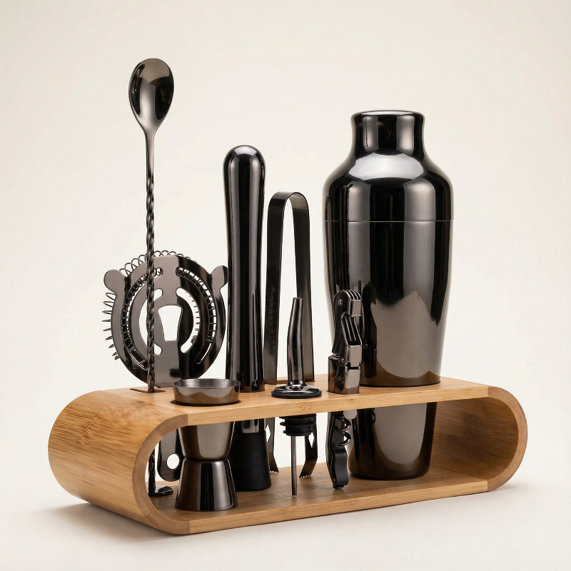 Set of black bar tools including a shaker, jigger, and spoon on a wooden stand against a beige background.