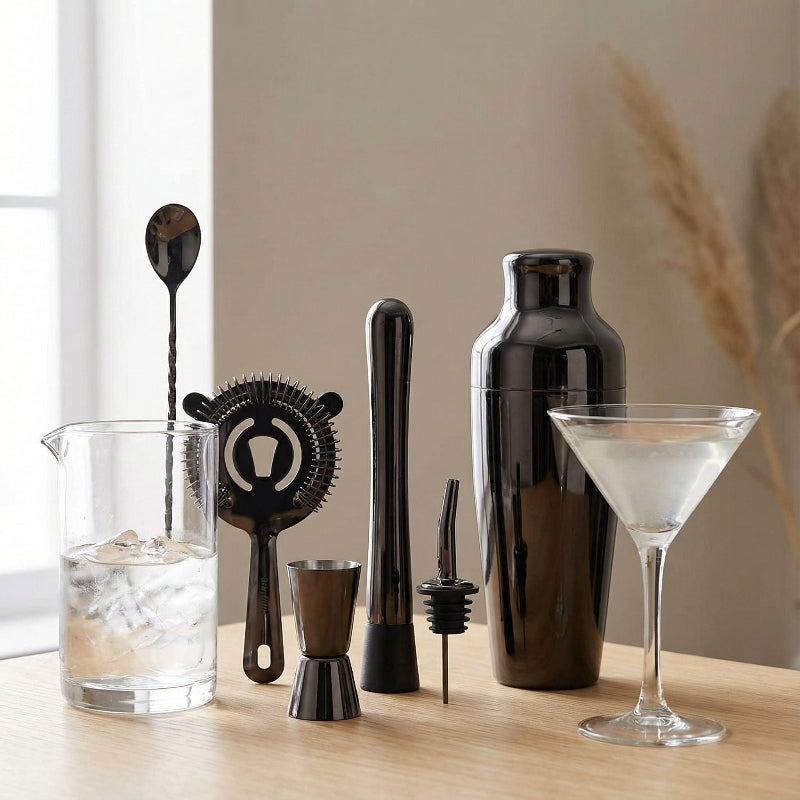 Bartending tools including a shaker, jigger, and strainer on a wooden surface with a glass of cocktail.