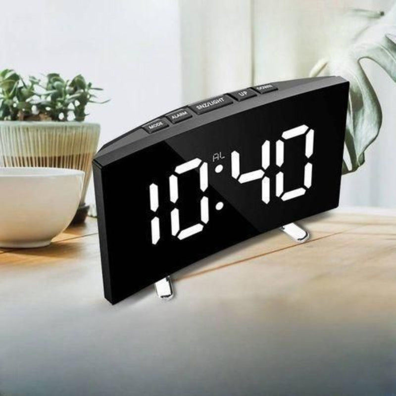 Digital clock on a table with plants in the background