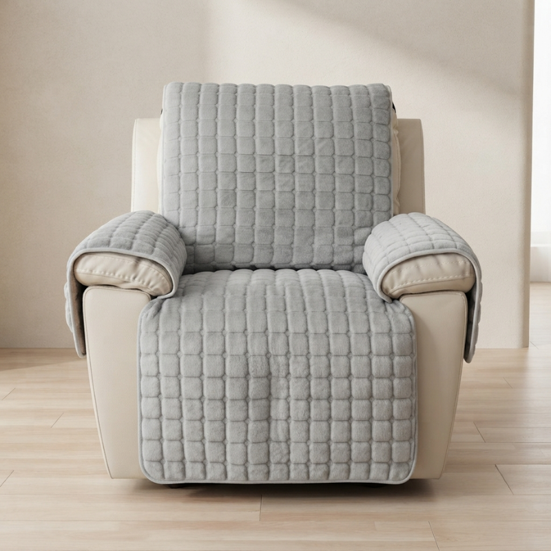 A light gray quilted slipcover with a textured grid pattern draped over a cream-colored recliner chair, set against a neutral beige wall and light wood floor.