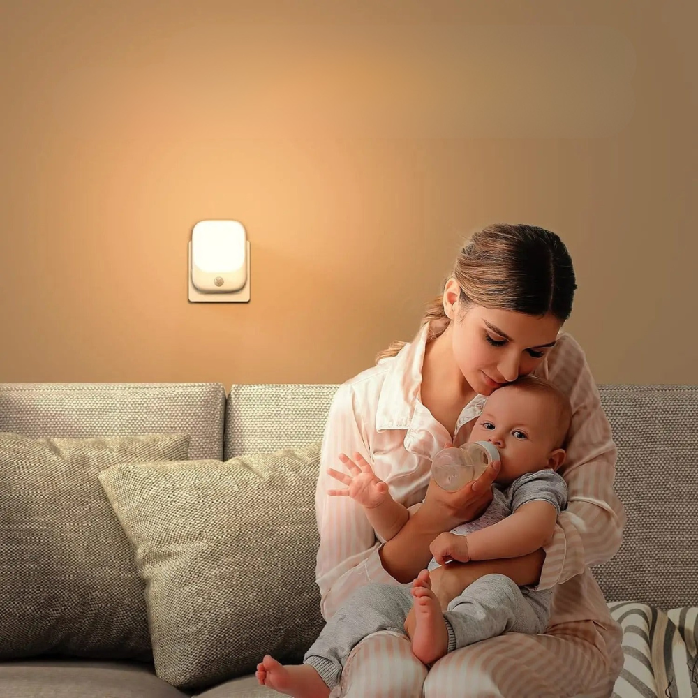Woman holding a baby in a cozy living room with a night light on the wall.