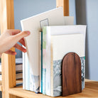 Hand opening a book with a wooden cover on a shelf.