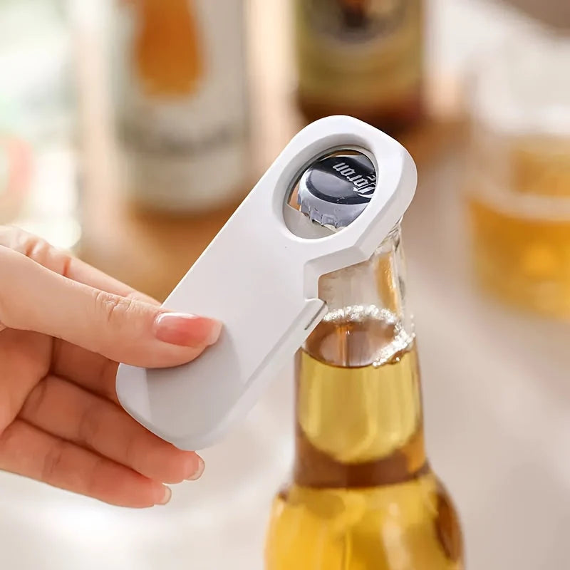 Hand using a white bottle opener on a beer bottle with a blurred background of bottles and glasses.