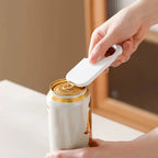 Hand using a can opener on a white can with a gold lid.
