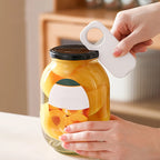 A person's hands are shown using a white plastic jar lifter tool to lift a heavy glass jar filled with sliced peaches, set against a softly blurred kitchen background.
