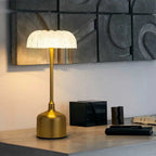 Gold table lamp on a wooden surface with decorative wall art in the background