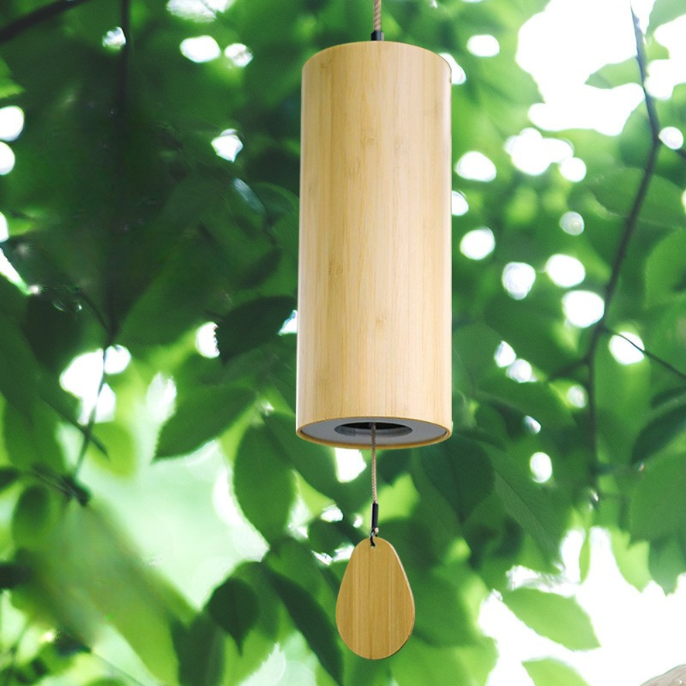Wooden cylindrical wind chime hanging against a green leafy background