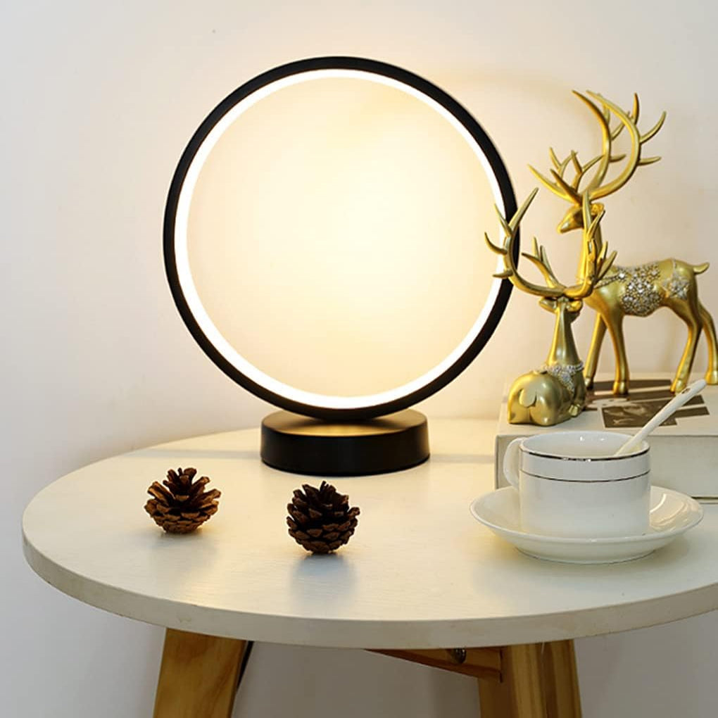 Round table with a lamp, cup, saucer, and decorative items on a neutral background