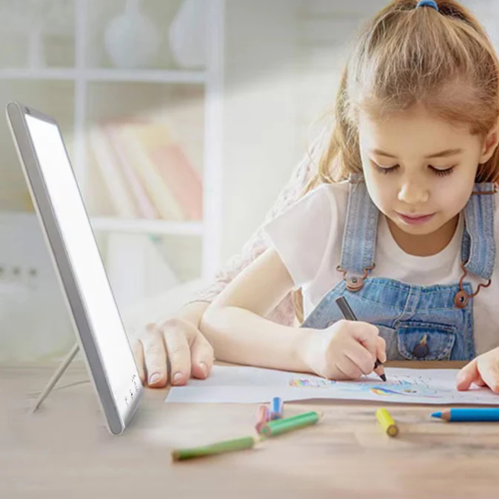 Child drawing at a desk with a lightbox and colored pencils.