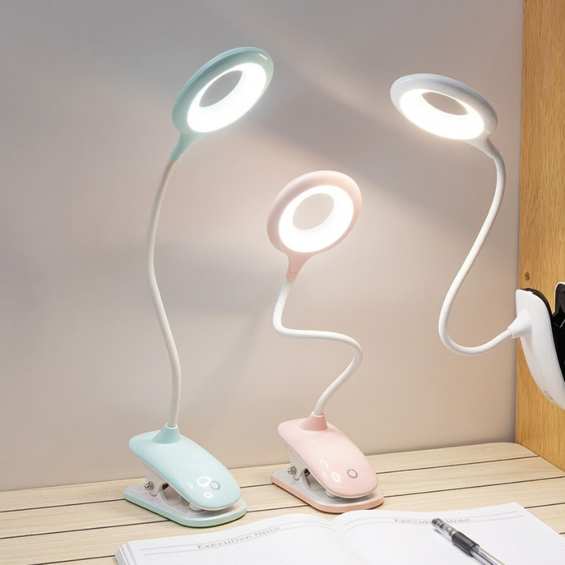 Three flexible desk lamps in different colors on a wooden surface with a white wall background.