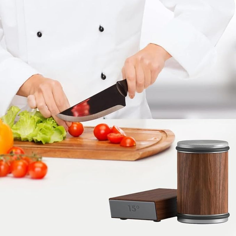 Person cutting vegetables on a cutting board with a knife, next to a wooden container and digital device.