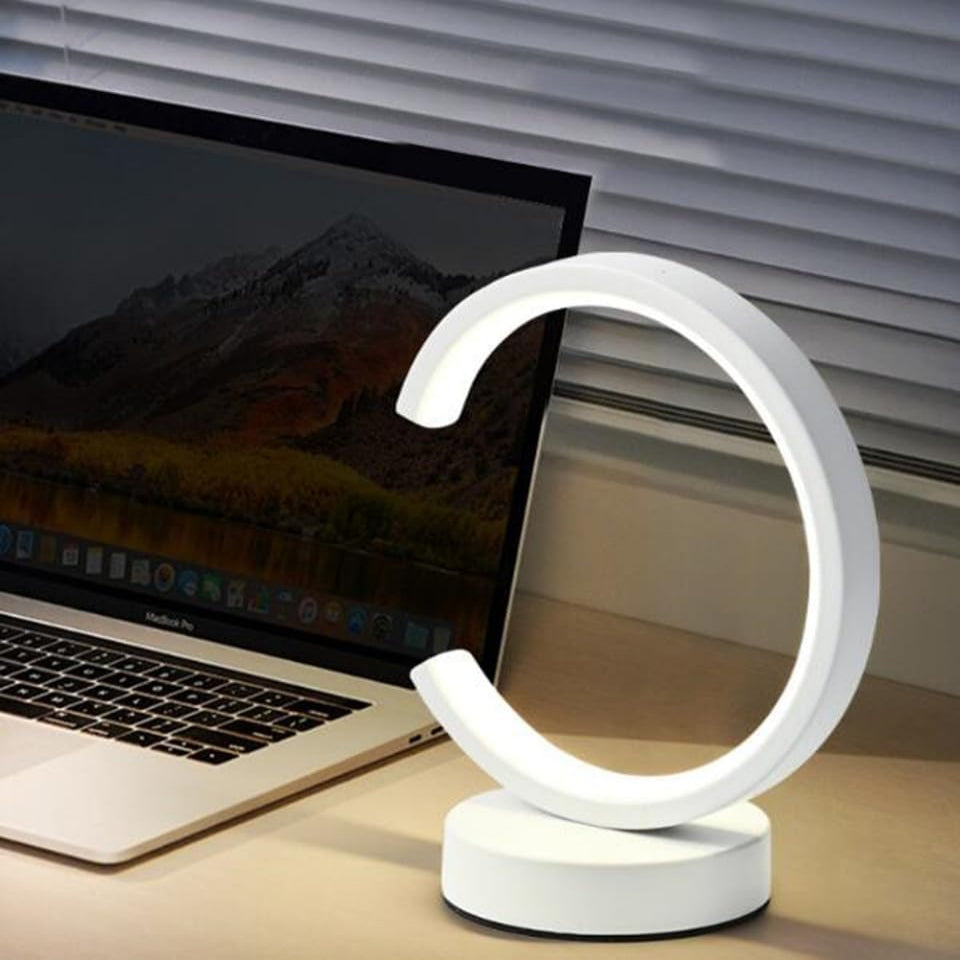 Modern desk lamp on a desk next to a laptop with a mountainous screen saver.