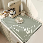 Green placemat with cartoon design on a kitchen counter with coffee machine and pastries.