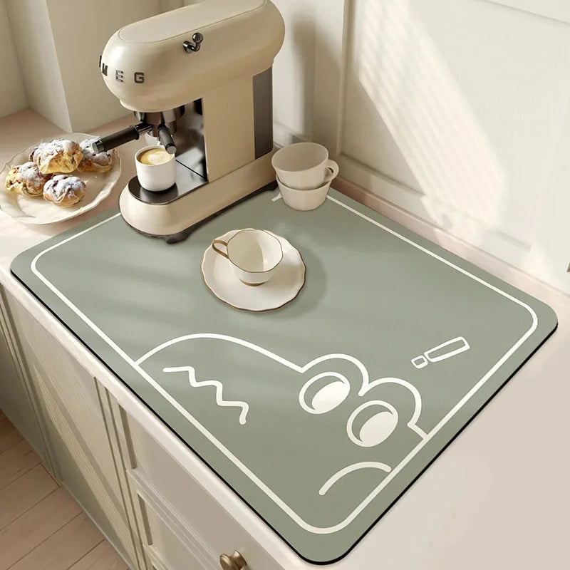 Green placemat with cartoon design on a kitchen counter with coffee machine and pastries.