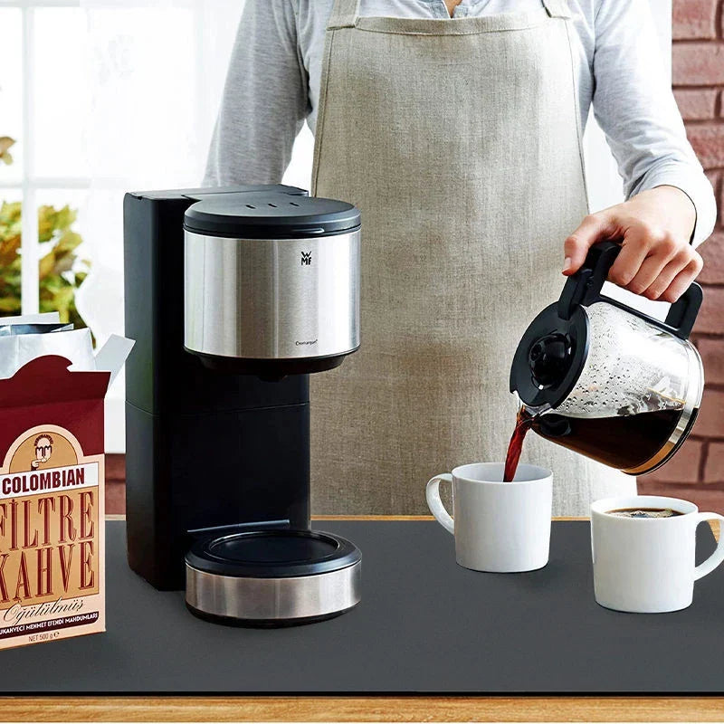 Person pouring coffee from a carafe into a cup next to a coffee maker and a bag of Colombian coffee beans.