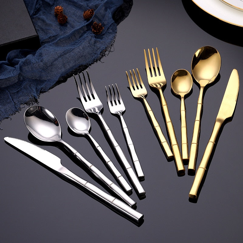 Set of gold and silver flatware on a dark surface with a blue napkin.