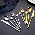 Set of gold and silver flatware on a dark surface with a blue napkin.