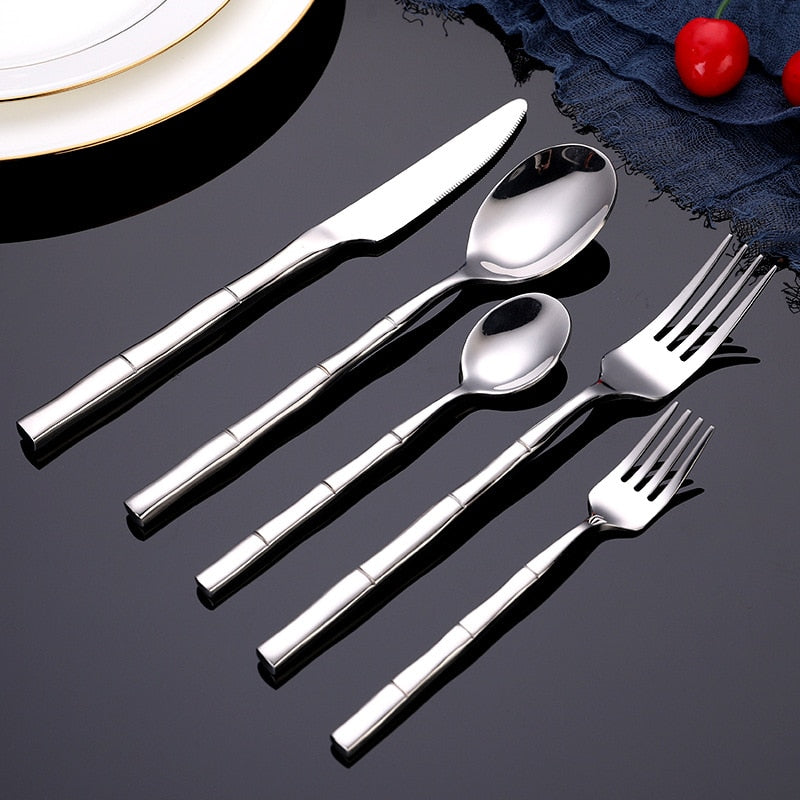 Set of silver cutlery including knives, spoons, and forks on a dark surface.