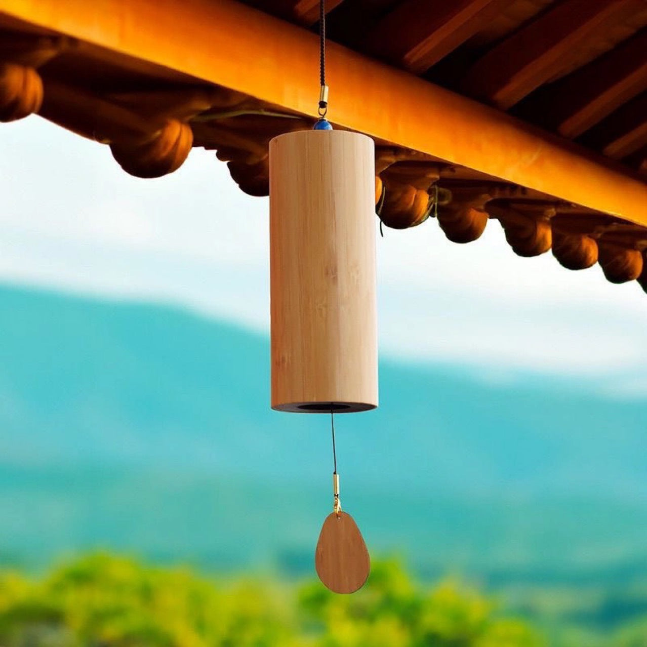 Wooden wind chime hanging from a wooden roof with a blurred natural background
