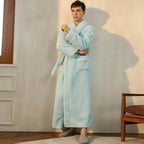 Man wearing a light blue robe standing in a room with a chair and window.