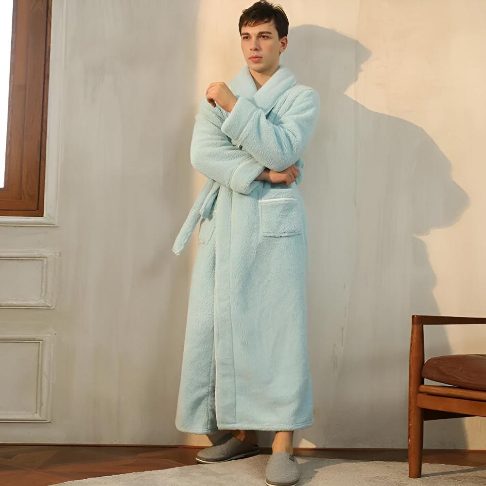 Man wearing a light blue robe standing in a room with a chair and window.