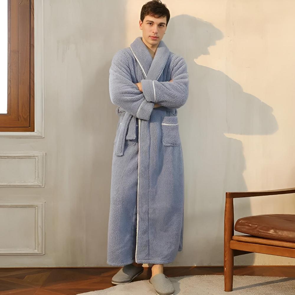Man wearing a blue robe standing in a room with a chair and window.