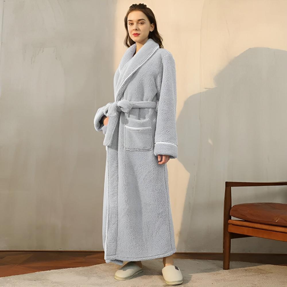 Woman wearing a gray bathrobe standing in a room with a chair and cushion.