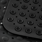 Close-up of a black textured rubber mat with raised circular bumps and drainage holes, layered over a similar mat in the background.