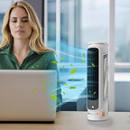 Woman using a laptop with a tower fan blowing air towards it in an office setting.