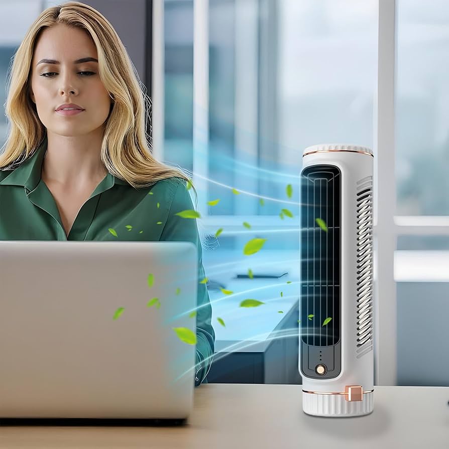 Woman using a laptop with a tower fan blowing air towards it in an office setting.