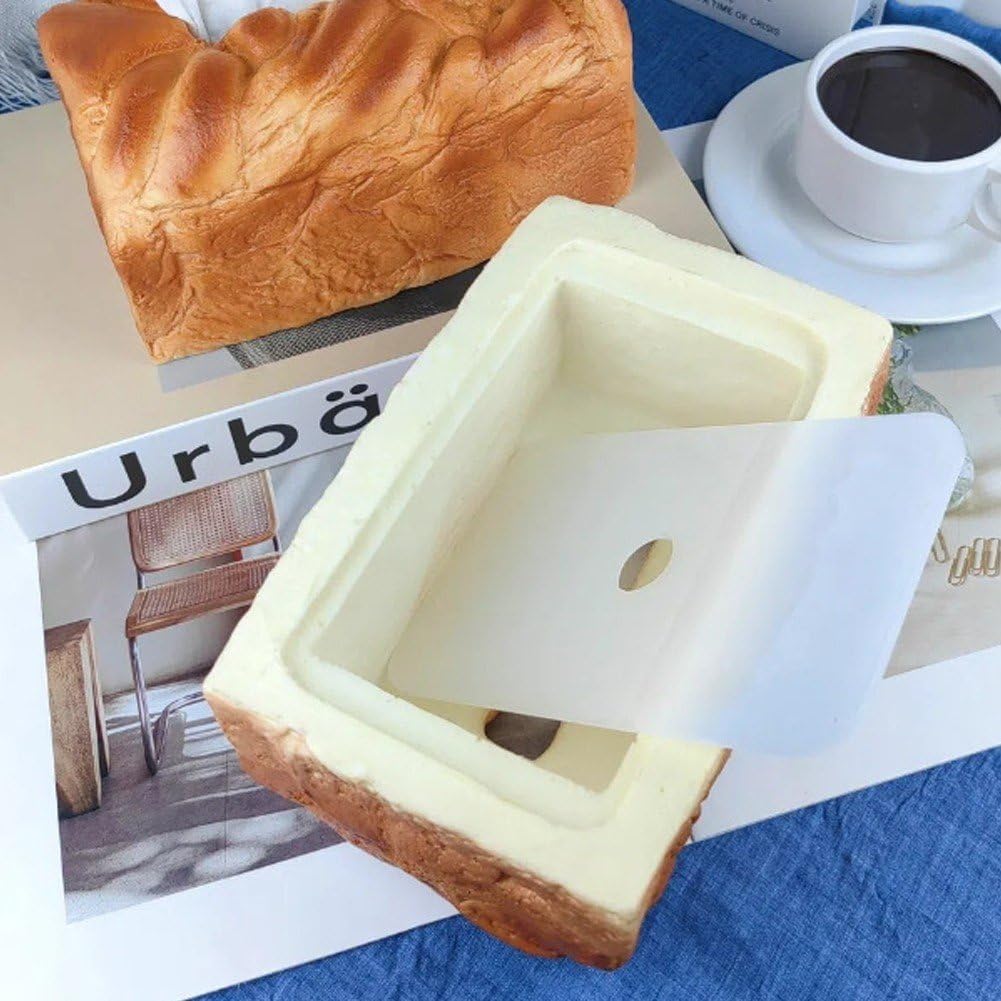 Square bread mold with a knife on top of a magazine with a coffee cup and loaf of bread in the background.