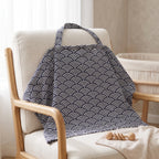 A fabric baby blanket with a navy blue and white wave pattern draped over a light beige upholstered wooden chair in a softly lit nursery setting.