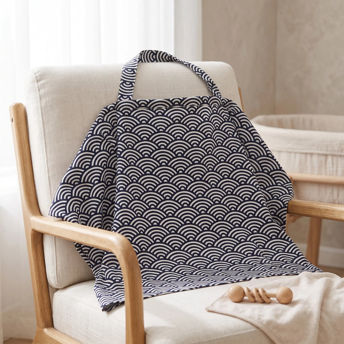 A fabric baby blanket with a navy blue and white wave pattern draped over a light beige upholstered wooden chair in a softly lit nursery setting.