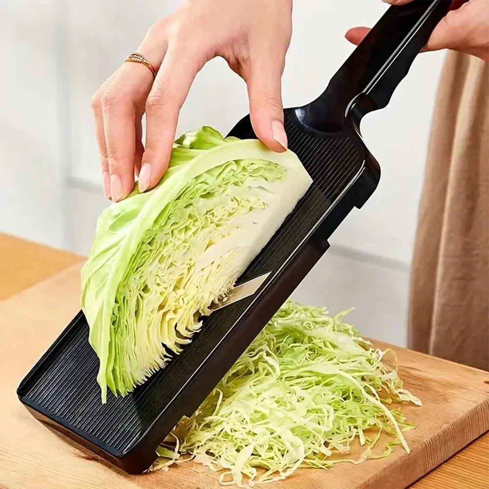 Person using a mandoline slicer to shred a head of cabbage on a wooden cutting board.