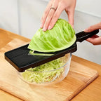 Person using a mandoline slicer to shred a head of cabbage into a clear bowl on a wooden cutting board.