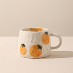 White ceramic mug with orange pumpkin designs on a beige background