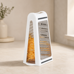 White box grater with shredded carrots on a light wooden surface