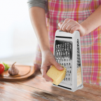 Person using a box grater to shred cheese on a wooden surface with a blurred background