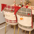 Two upholstered dining chairs decorated with festive snowman and Santa face covers, including red plaid Santa hats, red trim, and cream fabric faces, set in a decorated indoor dining area.