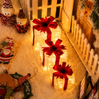 Three glowing rectangular Christmas gift box lights decorated with large red ribbon bows, arranged on a white faux-fur rug in a cozy holiday room setting with snowman decorations and warm ambient lighting.