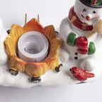 A close-up of a holiday-themed decorative light fixture or ornament featuring a snowman, a small red bird, and a flame-shaped socket on a white snowy base.