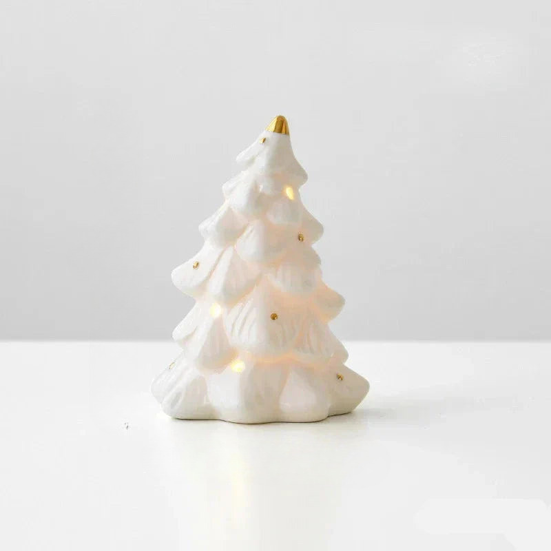 A white ceramic Christmas tree figurine with a gold finial on top and small gold dots, glowing with warm white string lights against a clean white background.