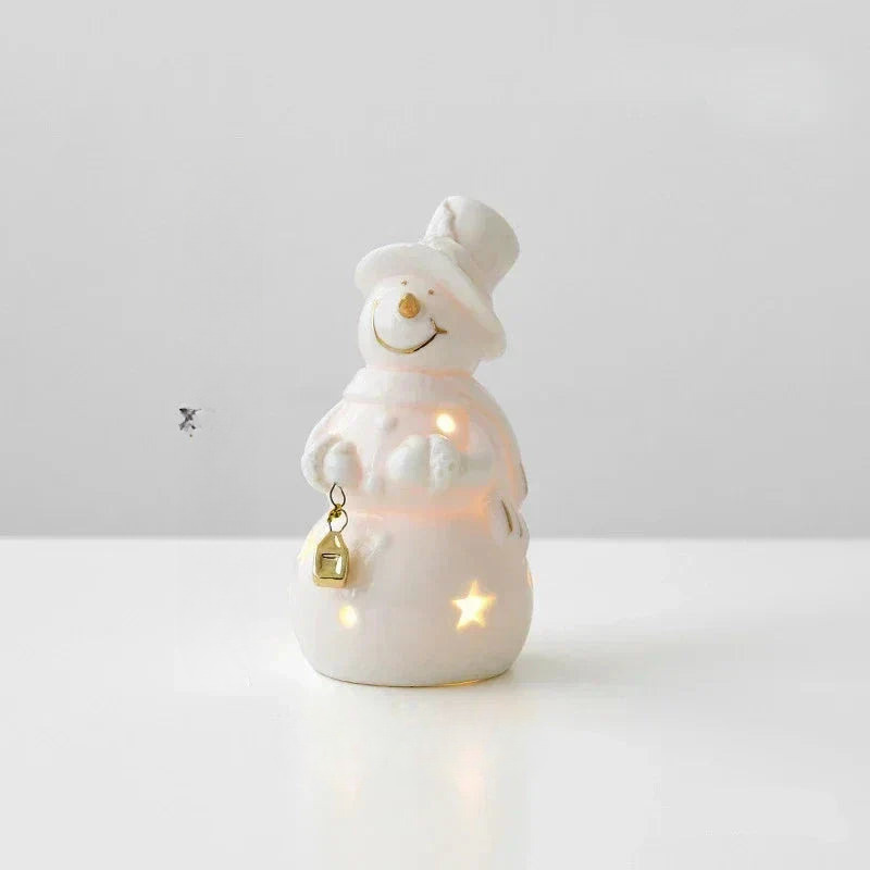 A white ceramic snowman figurine with warm internal lights, holding a small gold lantern, set against a clean white background.