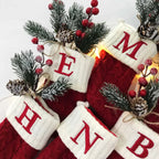 Red and white Christmas stockings with monogram letters, surrounded by festive decorations on a light background.
