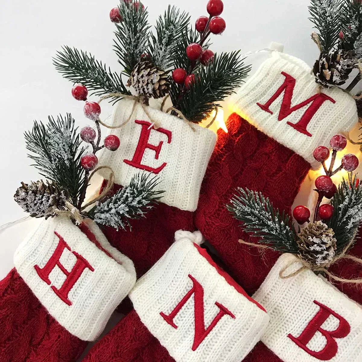 Red and white Christmas stockings with monogram letters, surrounded by festive decorations on a light background.