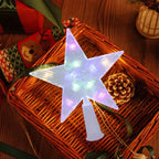 A glowing five-point star tree light with a white plastic base, displayed on a wicker basket with holiday decorations including a pinecone and ribbons.