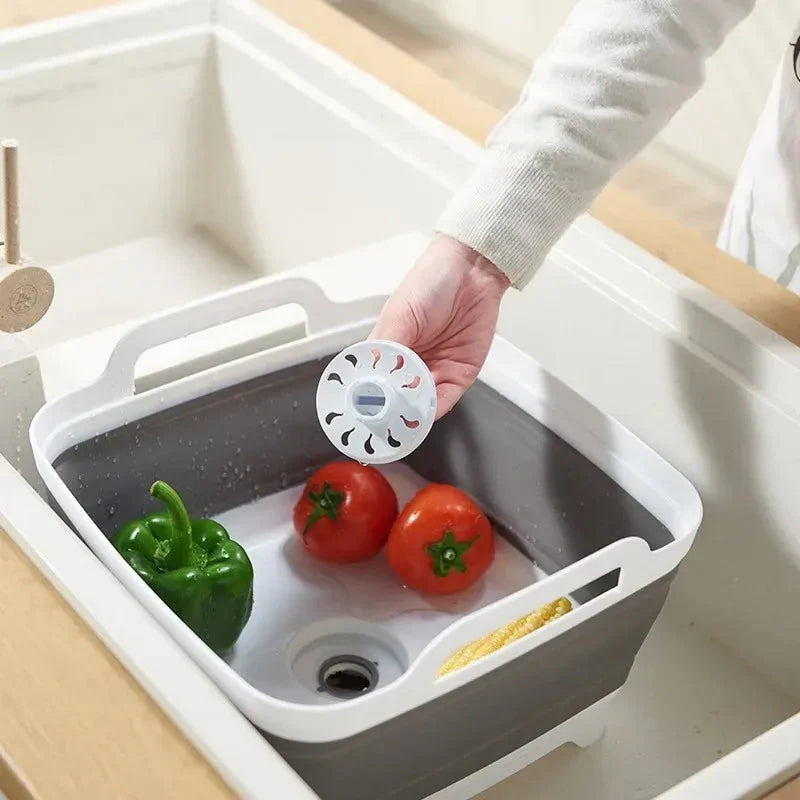 Collapsible kitchen sink with vegetables and a hand holding a white filter.
