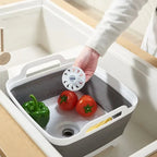 Collapsible kitchen sink with vegetables and a hand holding a white filter.