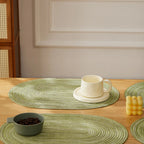 Green woven placemats on a wooden table with a cup and bowl.