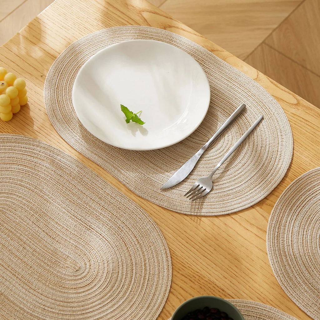 White plate with a fork and knife on woven placemats on a wooden table.